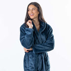 A woman wearing a plush teal waffle bathrobe with a shawl collar and tie belt, standing against a plain white studio background.