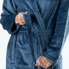 A close up of a woman wearing a plush teal waffle bathrobe against a plain white studio background.