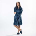 A woman wearing a plush teal waffle bathrobe with a shawl collar and tie belt, standing against a plain white studio background.