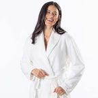 A woman wearing a white waffle bathrobe, smiling against a plain white background.