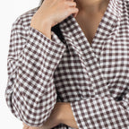 A close-up of a person wearing a brown and white gingham check wrap robe, with one hand adjusting the collar.