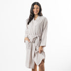 A woman modeling a long-sleeve gingham bathrobe with a tie belt and front pockets, photographed against a clean white studio background.