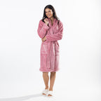 A woman wearing a plush pink bathrobe and white slippers, standing against a clean white studio background.