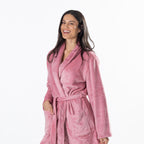 A woman wearing a pink waffle-textured plush bathrobe, smiling against a solid white background.