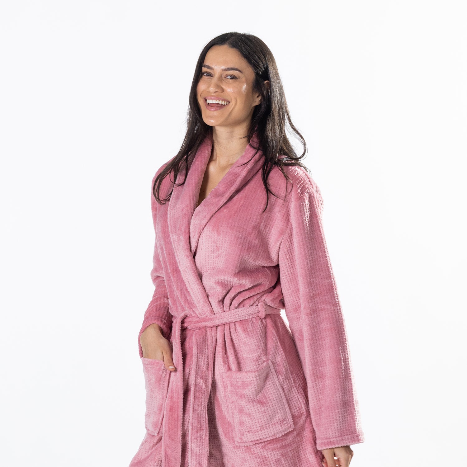 A woman wearing a pink waffle-textured plush bathrobe, smiling against a solid white background.