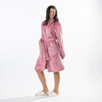 A woman modeling a plush pink bathrobe with a tie belt and front pockets, paired with white slippers, against a clean white studio background.