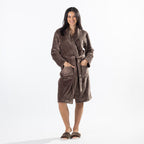 A woman modeling a brown waffle bathrobe against a plain white studio background.