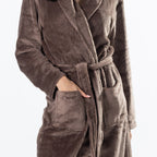 A person wearing a brown waffle-textured bathrobe with a matching tie belt and front patch pockets, shown against a plain light background.