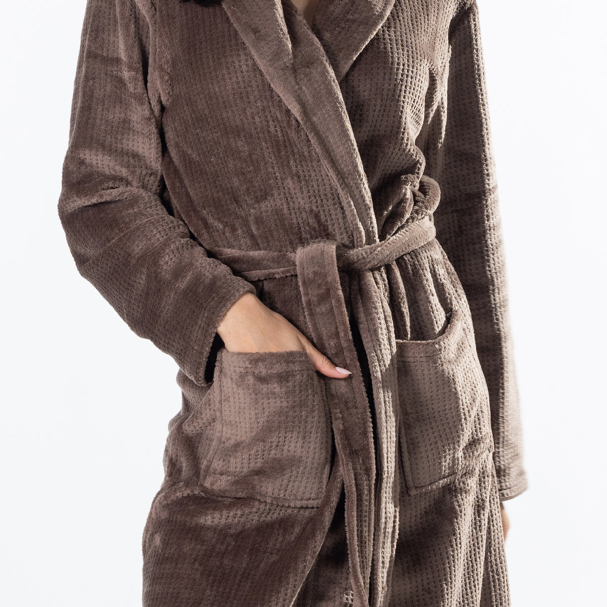 A person wearing a brown waffle-textured bathrobe with a matching tie belt and front patch pockets, shown against a plain light background.
