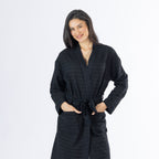 Mid-length front view of a model wearing the black textured bathrobe, showing the wrap neckline, self-tie belt and two front patch pockets.