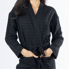 Close-up of the black textured bathrobe showing the subtle stripe texture, wrap neckline, waist tie and front pocket detail.