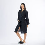 Full-length angled view of a model wearing the black textured bathrobe with one hand in the pocket and the robe tied at the waist.
