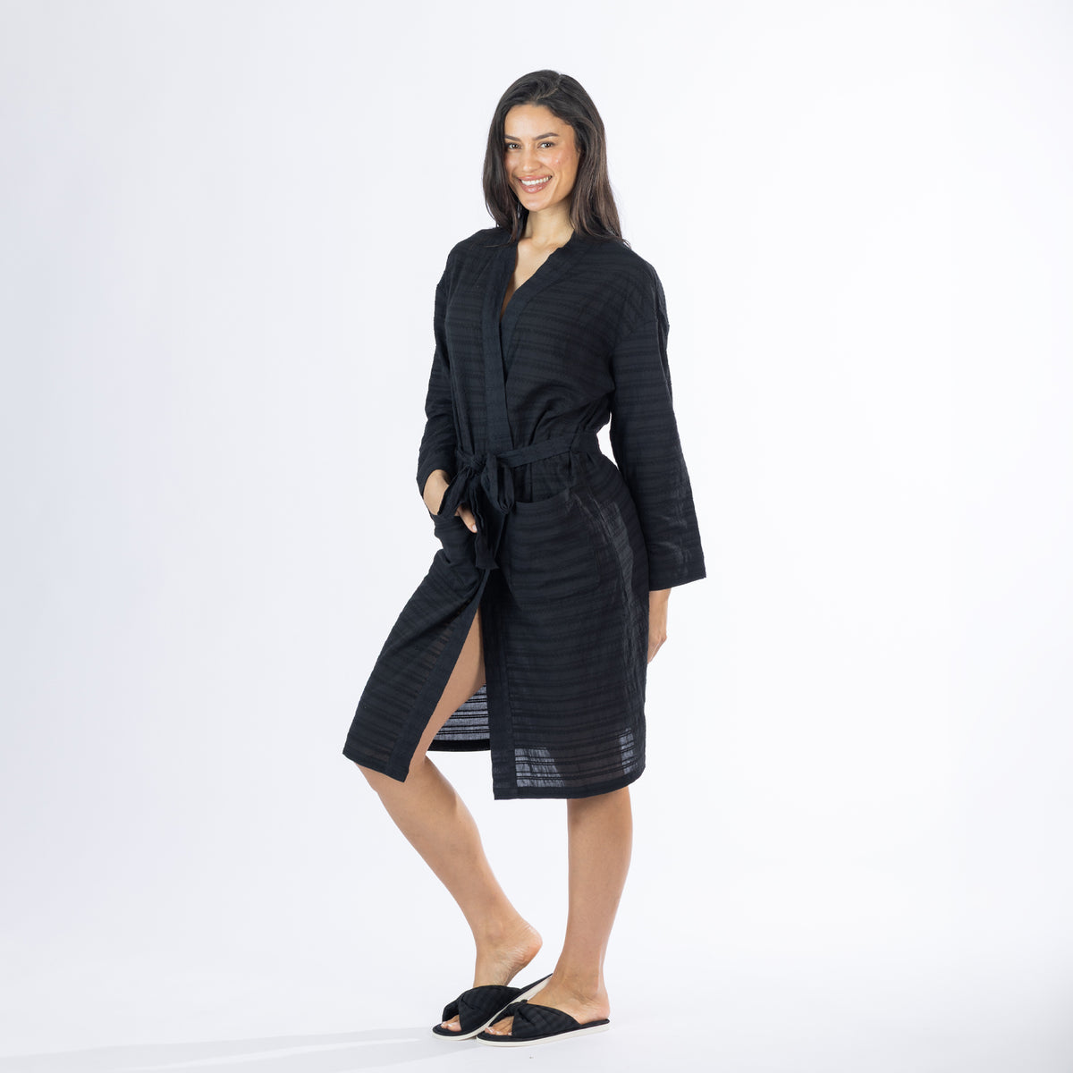 Full-length angled view of a model wearing the black textured bathrobe with one hand in the pocket and the robe tied at the waist.
