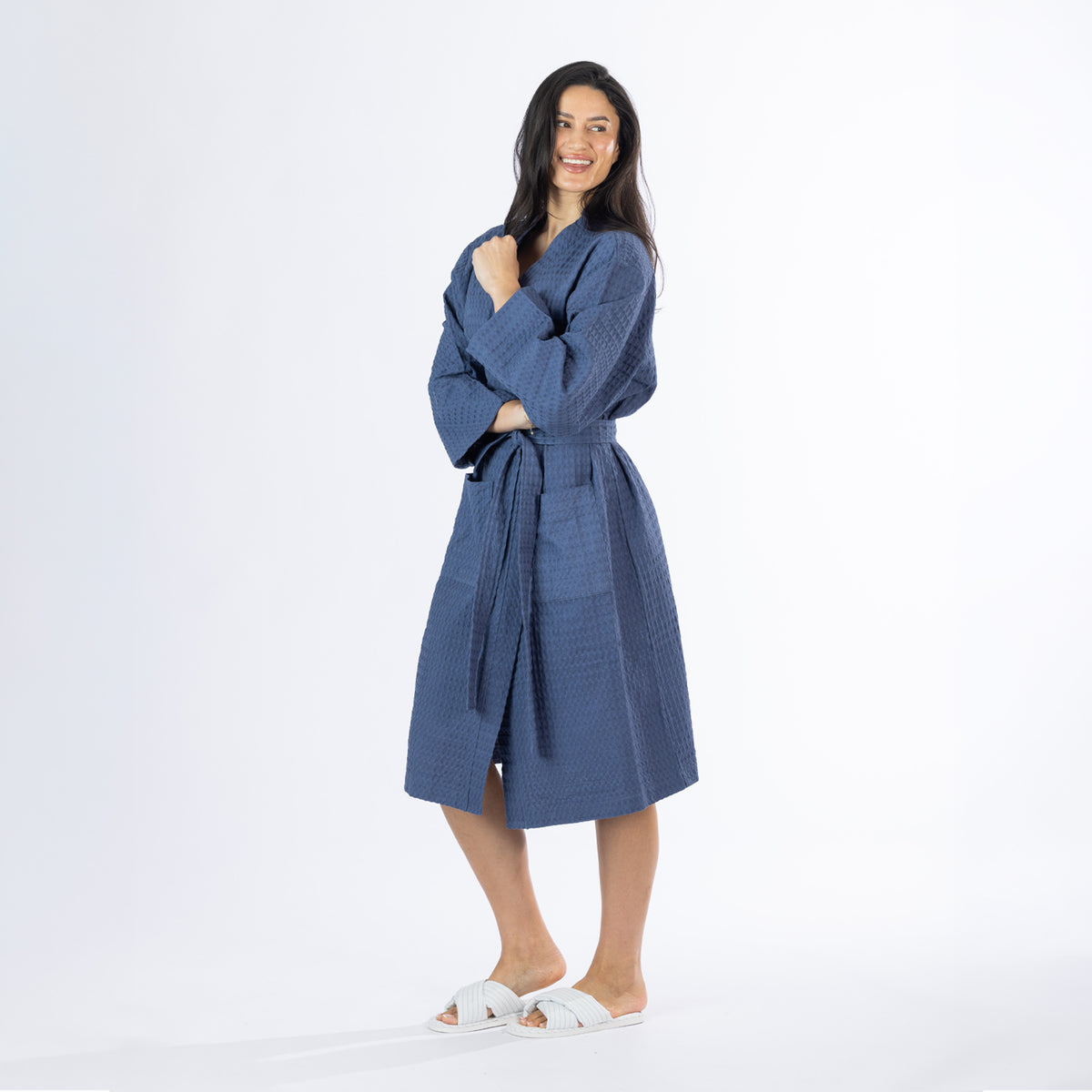 Model wearing an indigo Cove Dilys Waffle Bathrobe with textured fabric, long sleeves, front pockets and a waist tie belt.