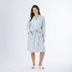 Full-length front view of a model wearing a pale blue textured stripe robe with a tie waist, long sleeves and front patch pockets, styled with slippers on a white background.