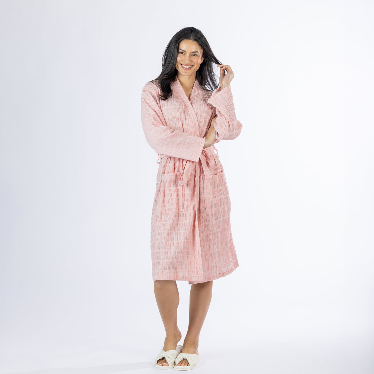 Full-length front view of a model wearing a pink textured stripe robe with a tie waist, long sleeves and front patch pockets, styled with slippers on a white background.