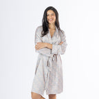 Amparo Cassie Satin Print Bathrobe in Pink modelled from the front, featuring a soft blush pink base with an all-over blue and neutral paisley print, long sleeves, a wrap front and matching waist tie.