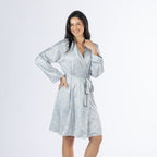 Amparo Cassie Satin Print Bathrobe in Denim modelled from the front at a slight angle, featuring the all-over paisley print, shawl collar, long sleeves and adjustable waist tie.