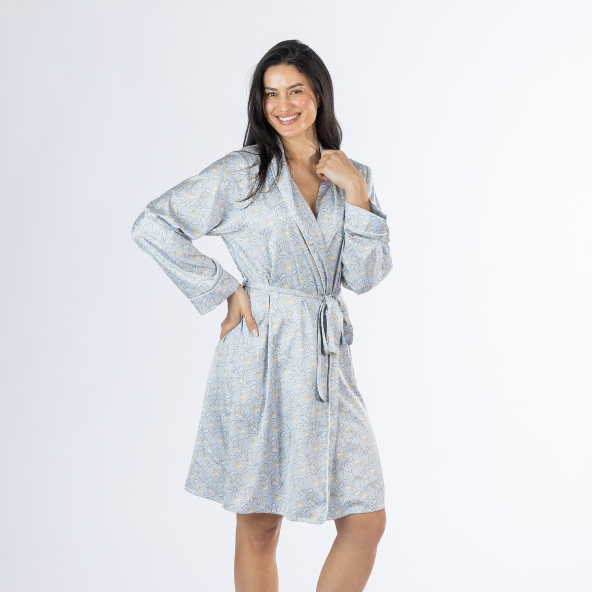 Amparo Cassie Satin Print Bathrobe in Denim modelled from the front at a slight angle, featuring the all-over paisley print, shawl collar, long sleeves and adjustable waist tie.