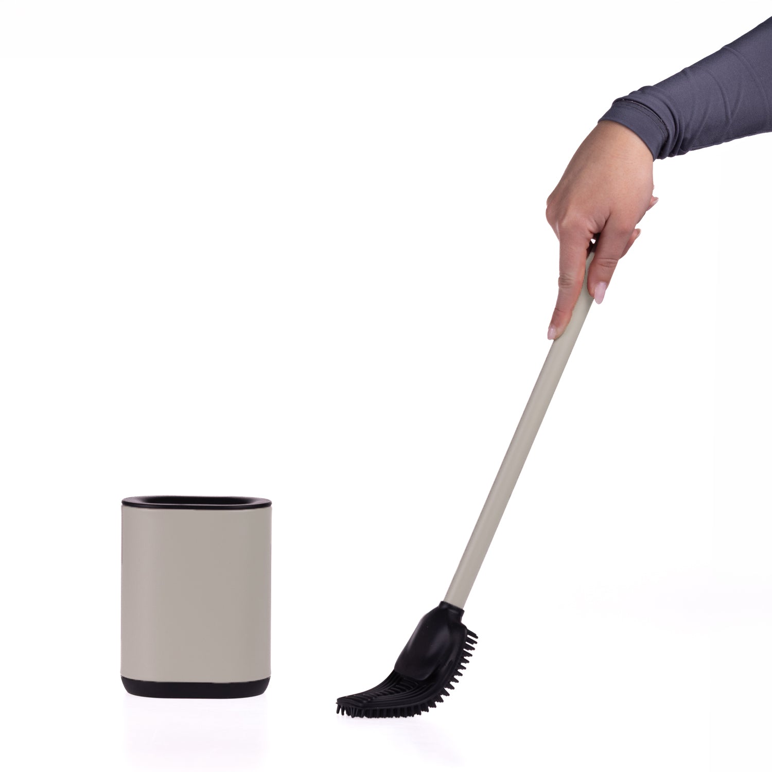A hand holding a long-handled black and taupe cleaning brush next to a matching taupe and black cylindrical holder on a white background.