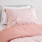 Kids floral print duvet cover set pillowcase with small scattered flowers and leaves styled on a white metal bed in a neutral bedroom.