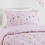 Pale pink kids fairy print fabric with small illustrated fairies, flowers, and delicate leaf details designed on a bed.