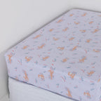 Purple fitted sheet with bunnies and flowers on a white mattress.