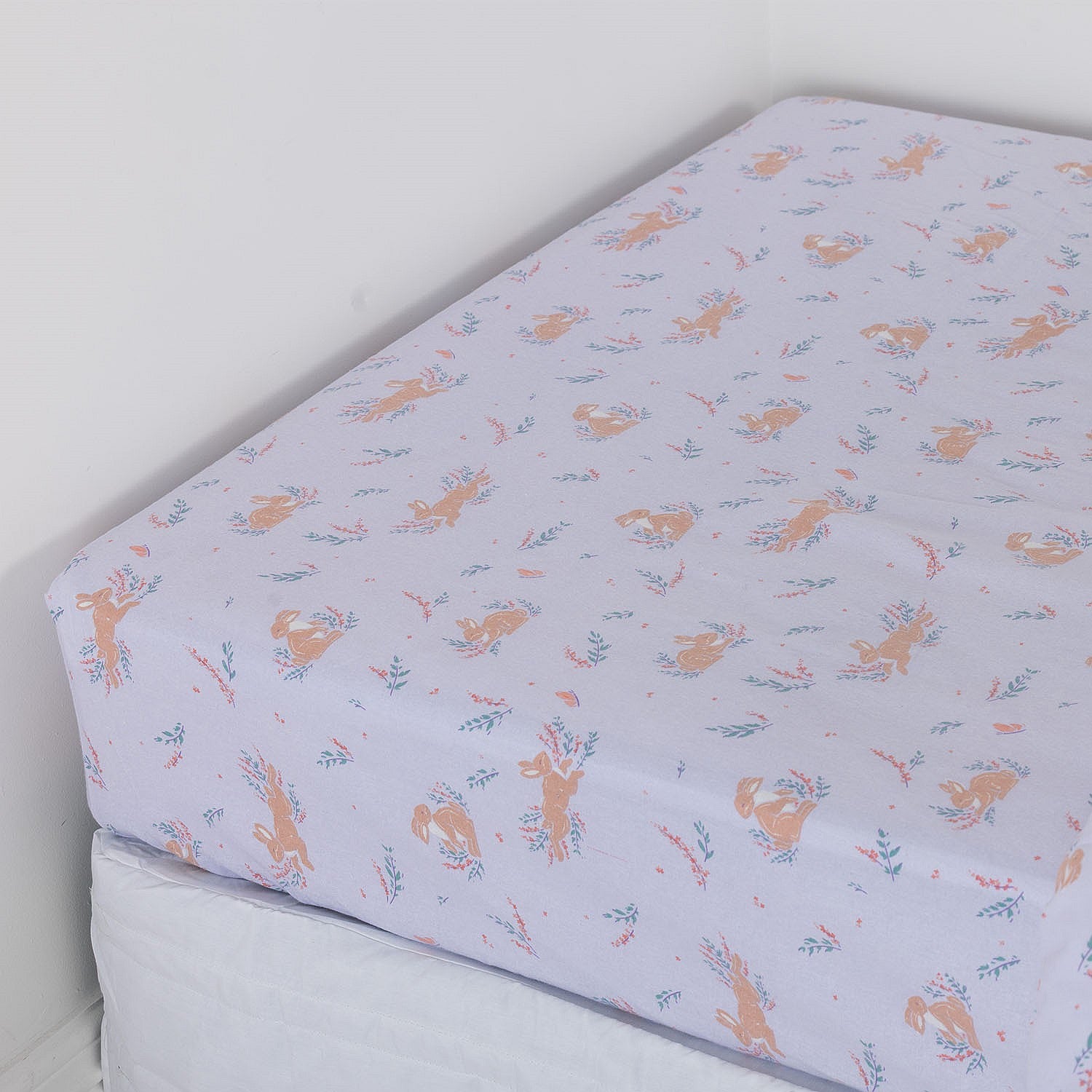 Purple fitted sheet with bunnies and flowers on a white mattress.