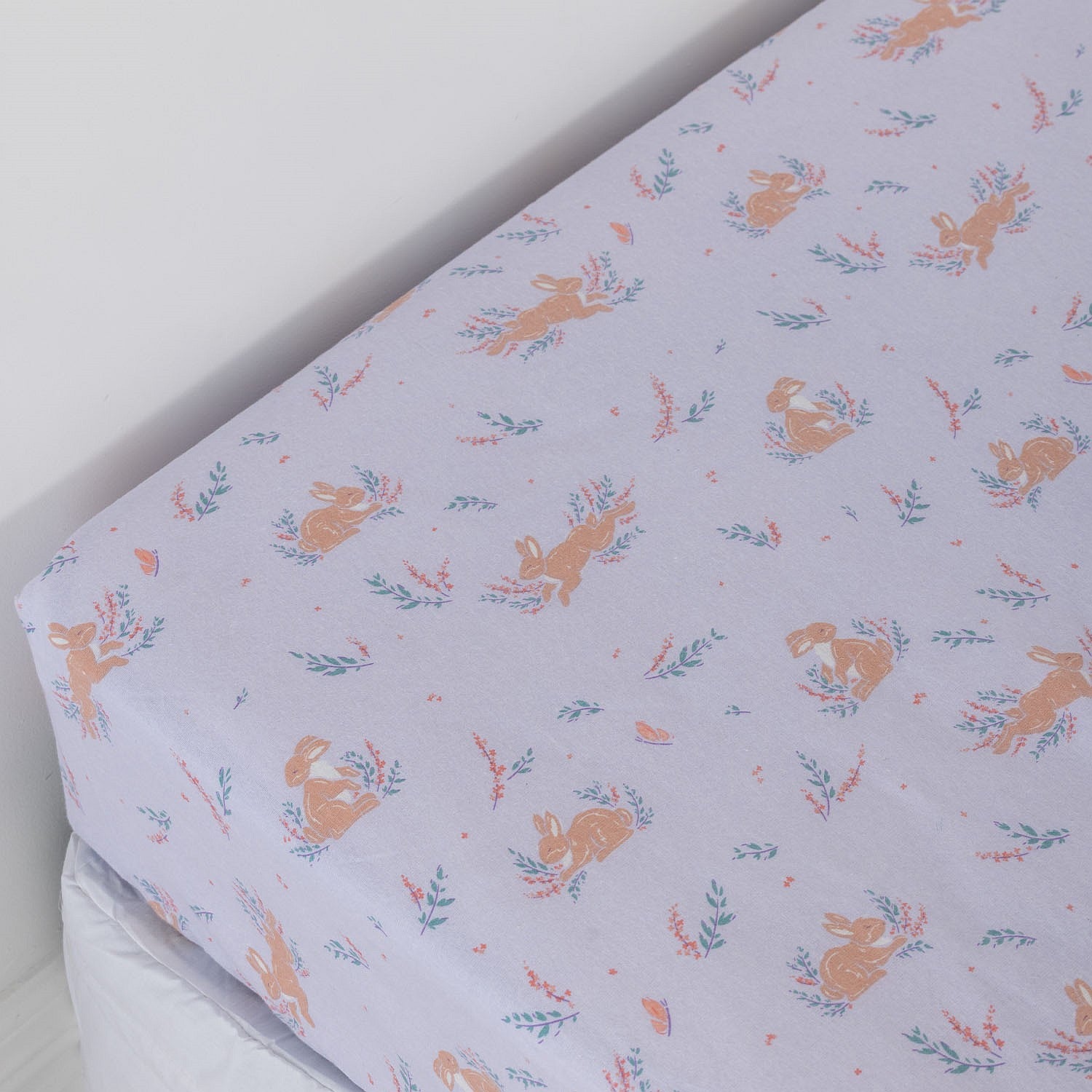 Purple fitted sheet with bunnies and flowers on a white mattress.