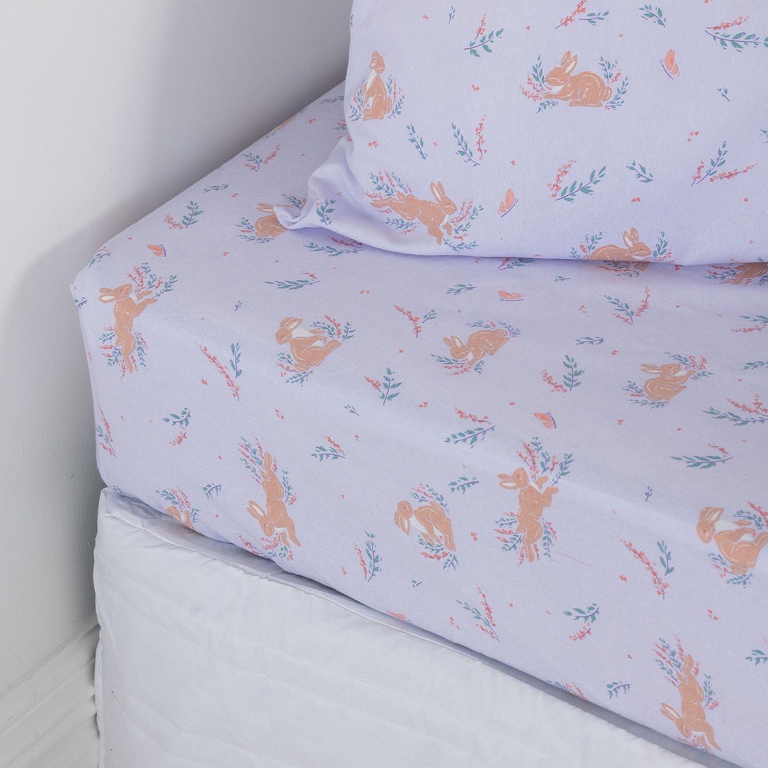 Purple fitted sheet with bunnies and flowers on a white mattress with a matching pillowcase