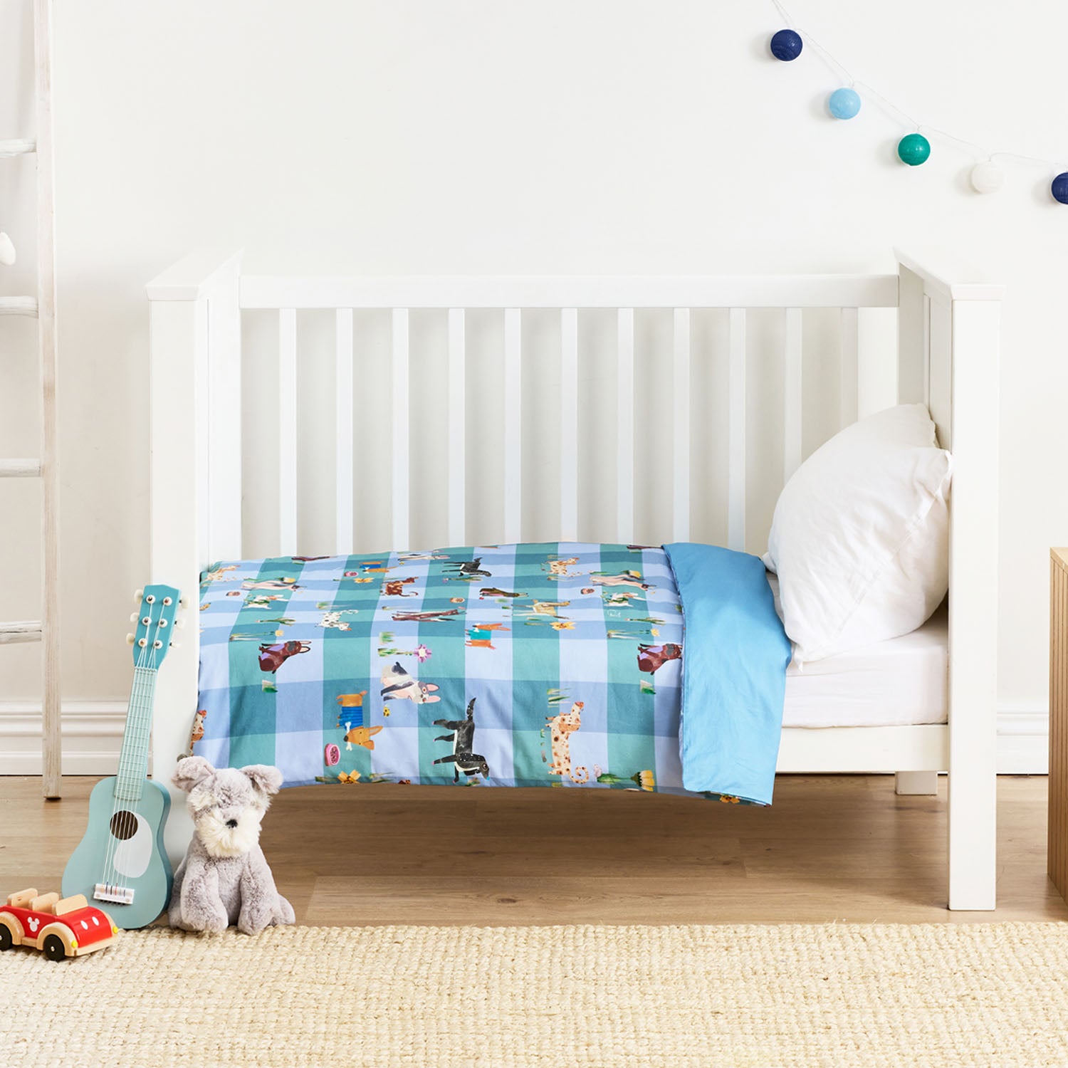 Baby cot styled with a blue patterned cot duvet and white pillow in a nursery room.