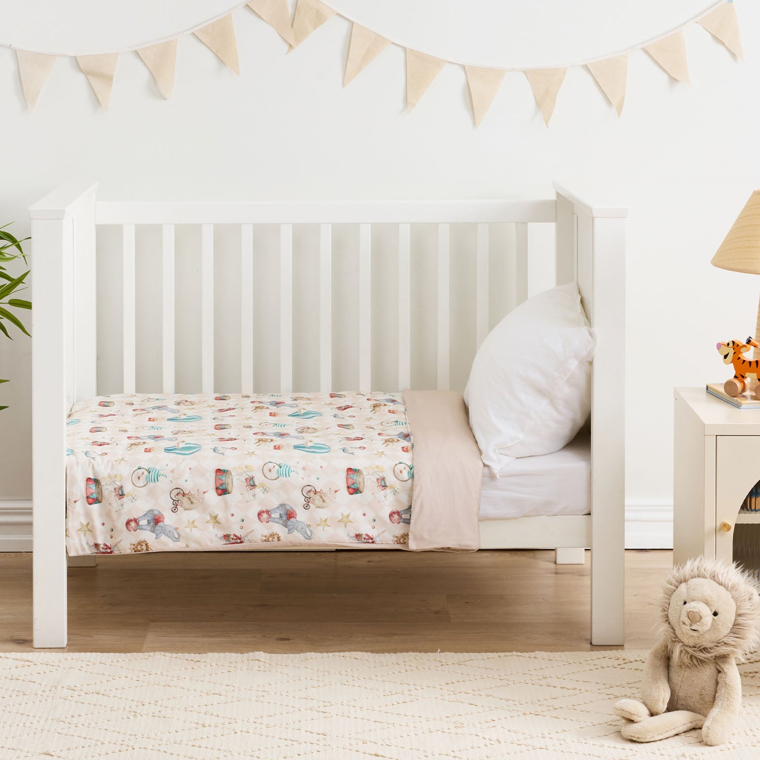 Baby cot styled with a carnival pattern and white pillow in a neutral nursery room.