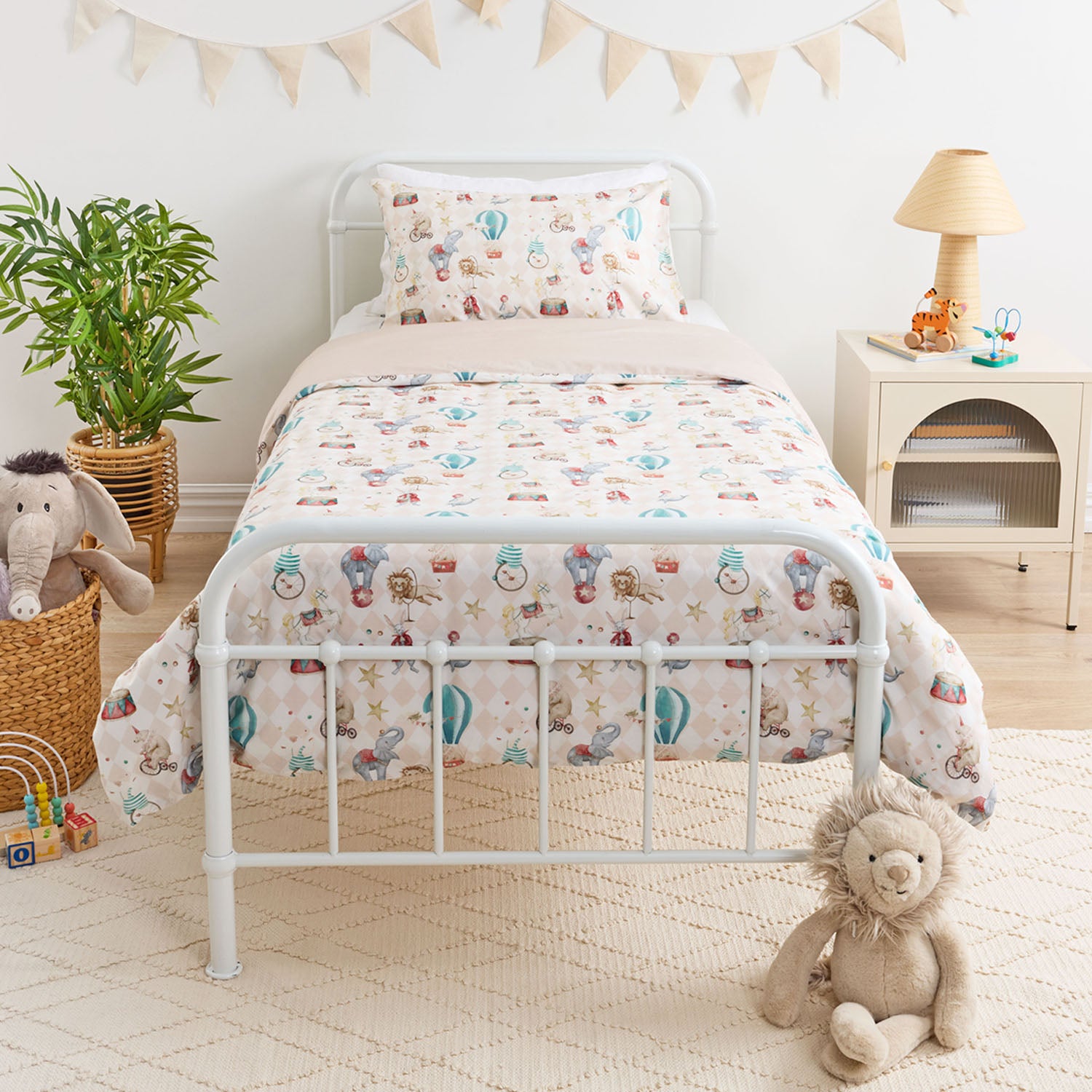 Kids carnival patterned duvet cover set styled on a white metal bed in a neutral bedroom.