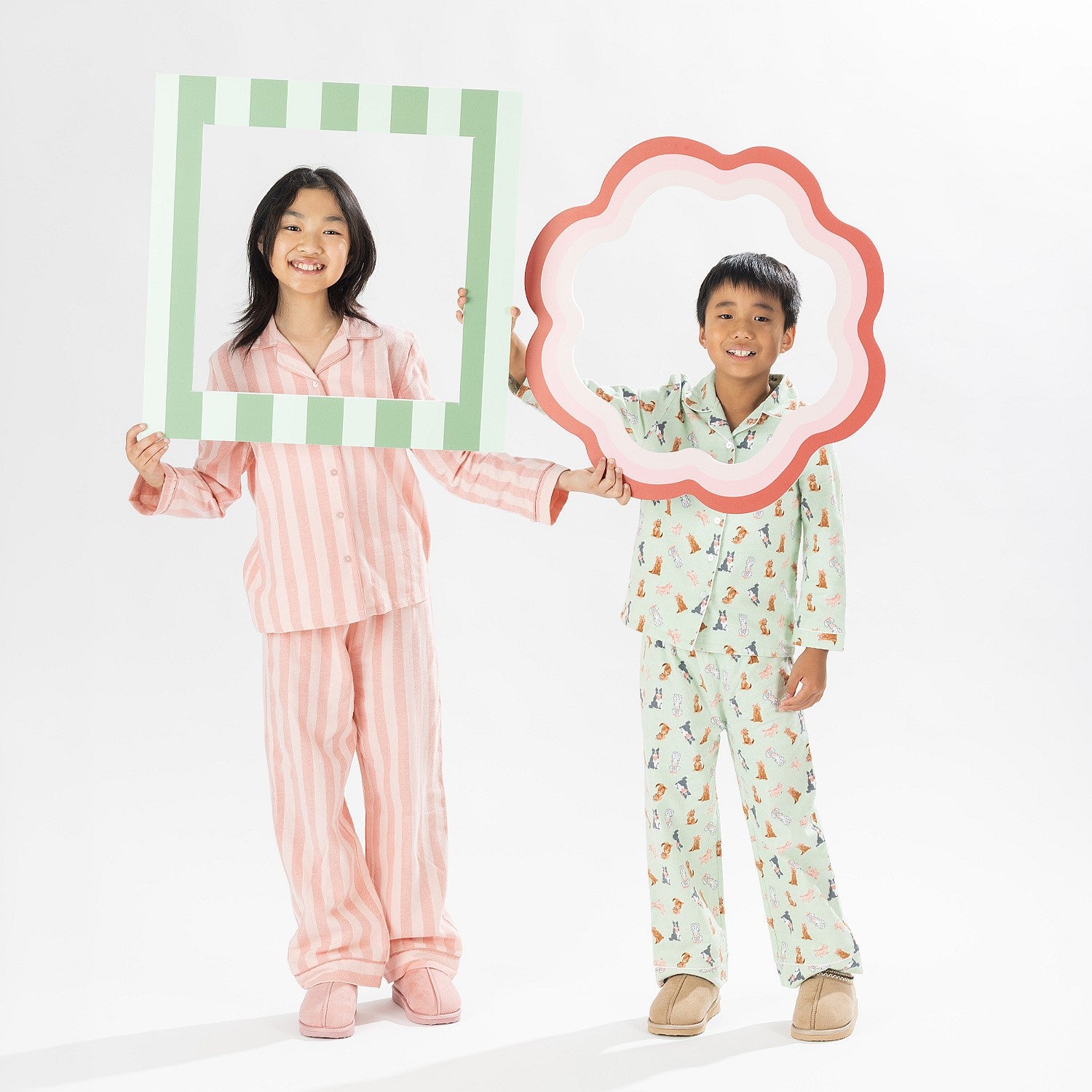 Two children wearing printed pyjama sets, one in pink stripes and one in green dog print, holding picture frame props.