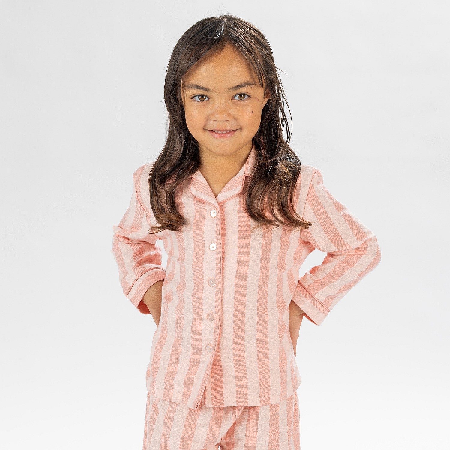 Child wearing pink striped flannelette pyjamas on a white background.