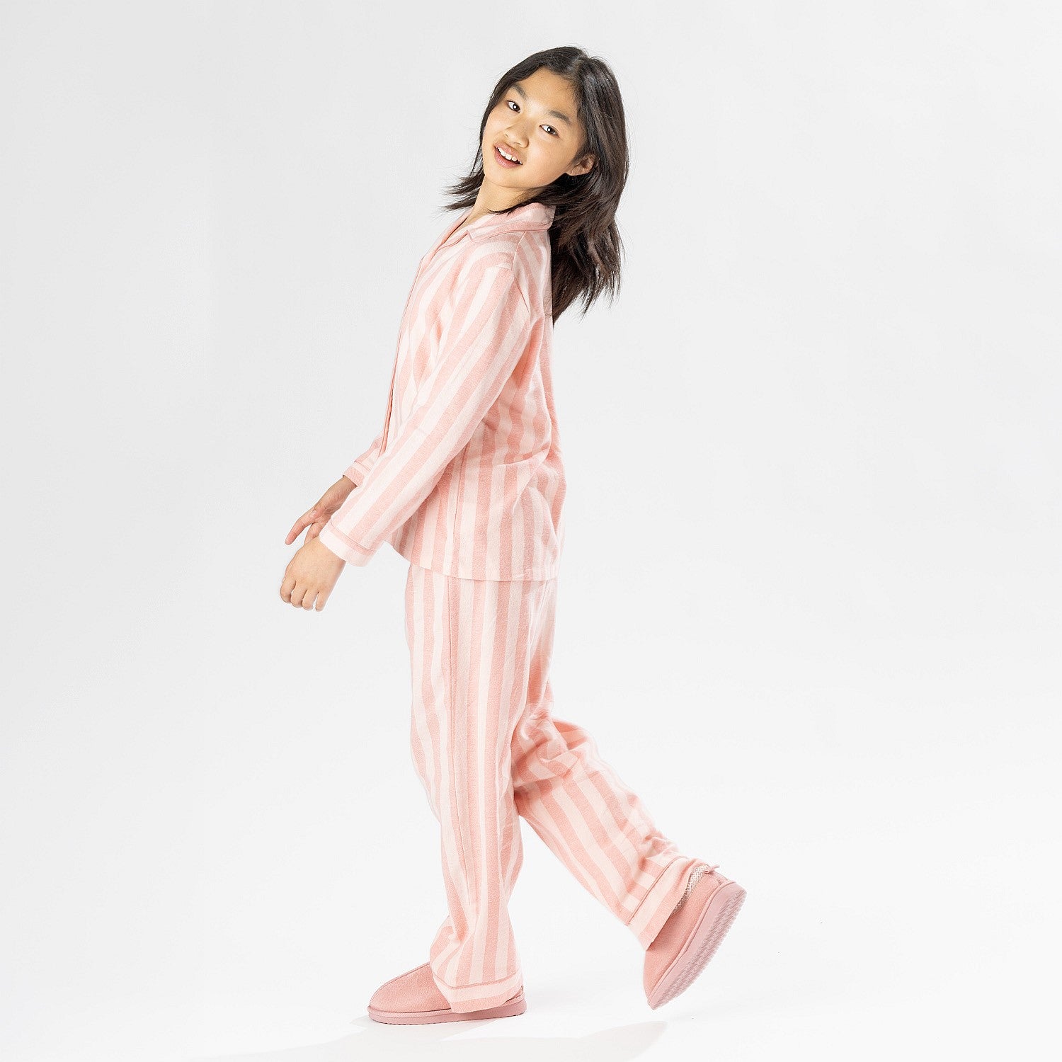 Child wearing pink striped flannelette pyjamas on a white background.