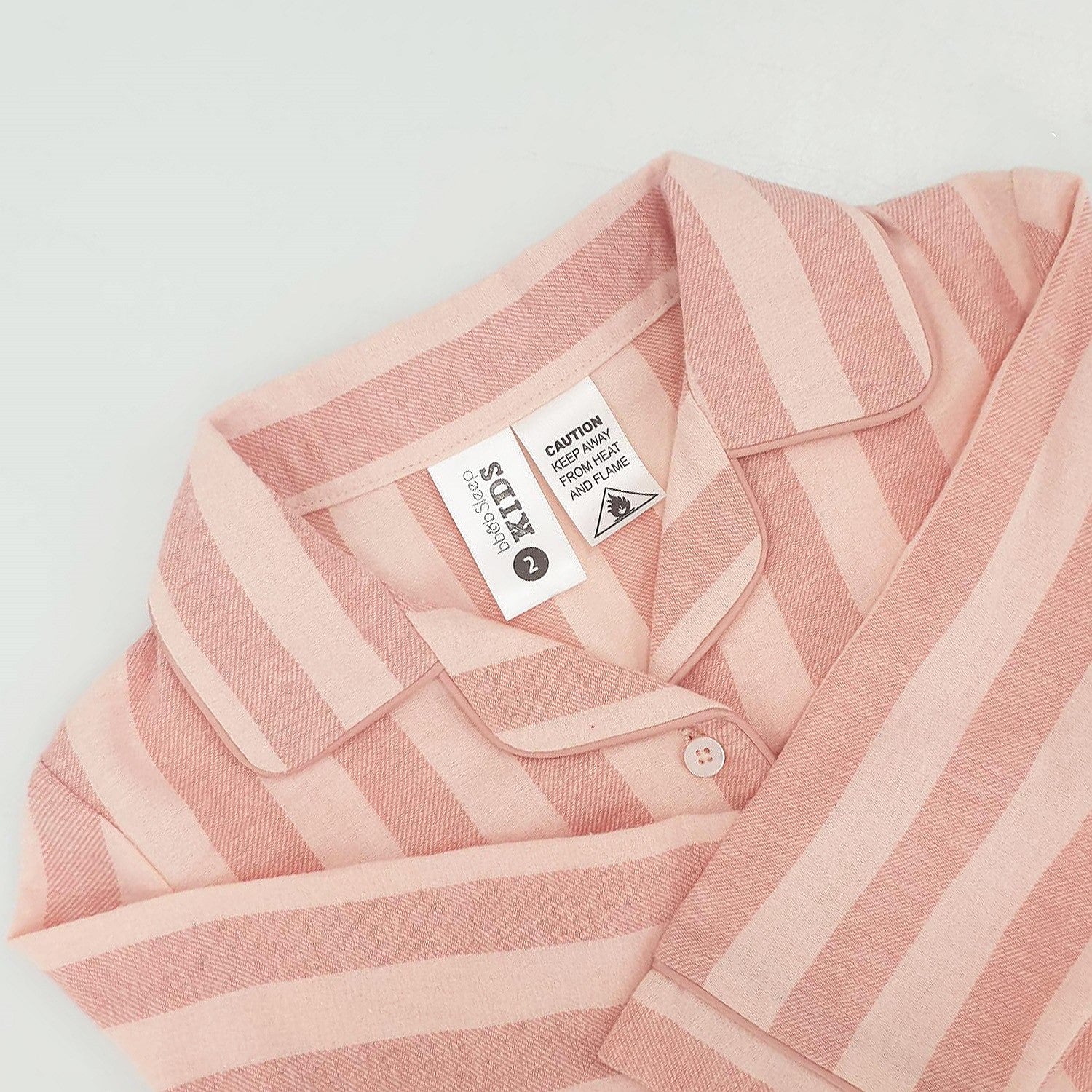 close up of pink striped flannelette pyjamas on a white background showing the tag and caution label