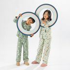 Two children wearing playful printed pyjama sets, one in green and one in light green, holding picture frame props.