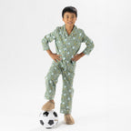 Child wearing green soccer print pyjamas standing with a soccer ball on a white background.