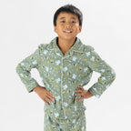 Child wearing green soccer print pyjamas standing on a white background.