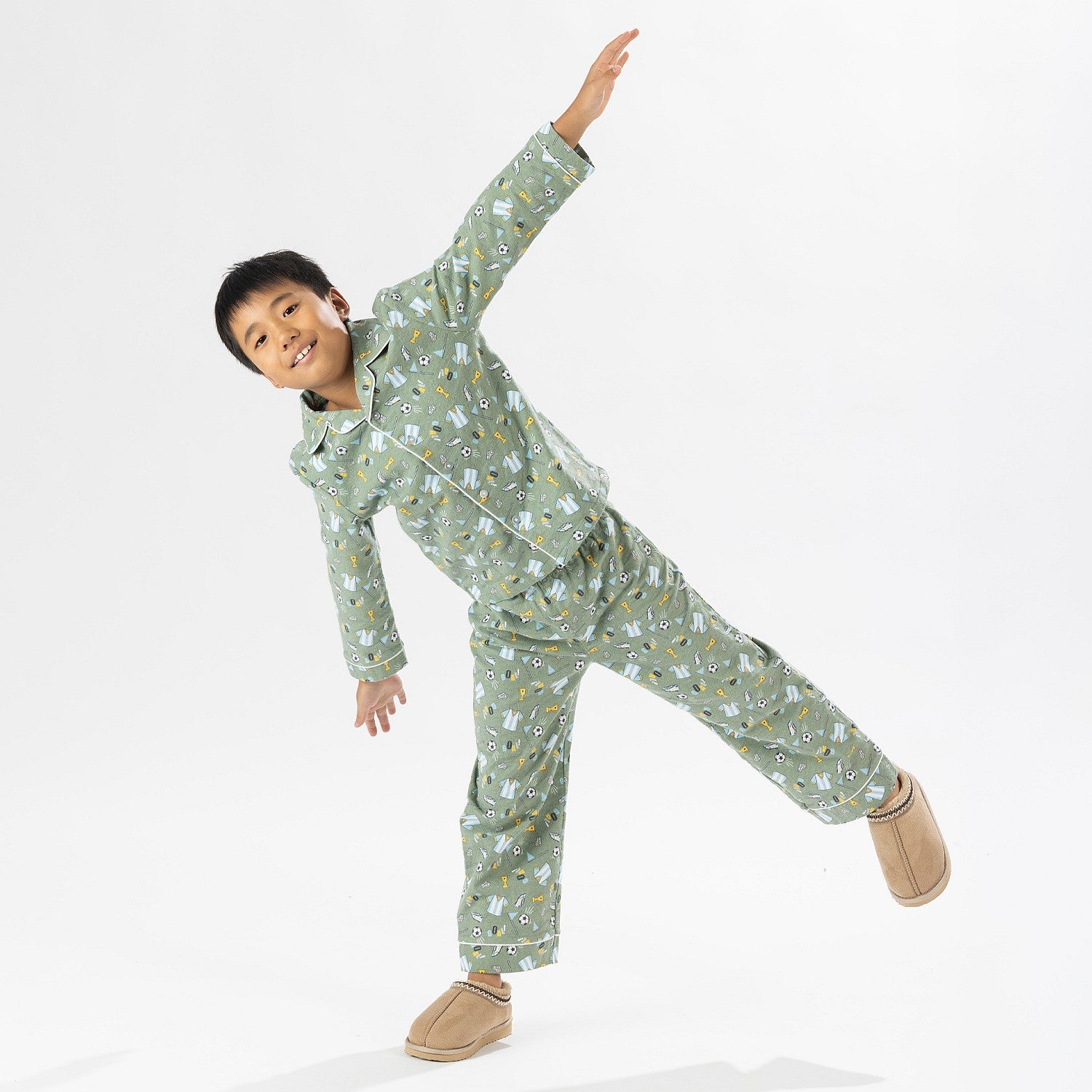 Child wearing green soccer print pyjamas standing on a white background.