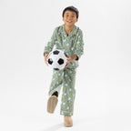 Child wearing green soccer print pyjamas standing with a soccer ball on a white background.
