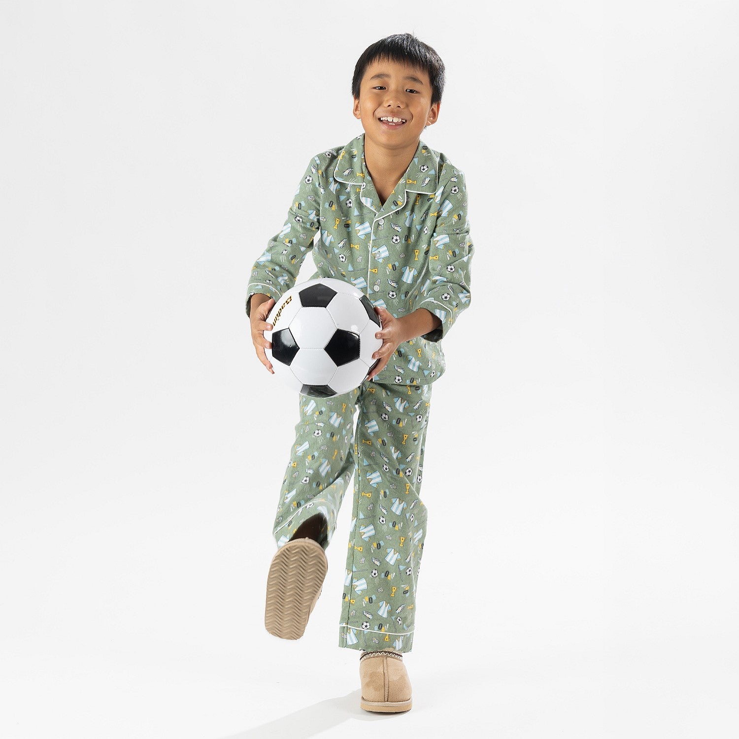 Child wearing green soccer print pyjamas standing with a soccer ball on a white background.