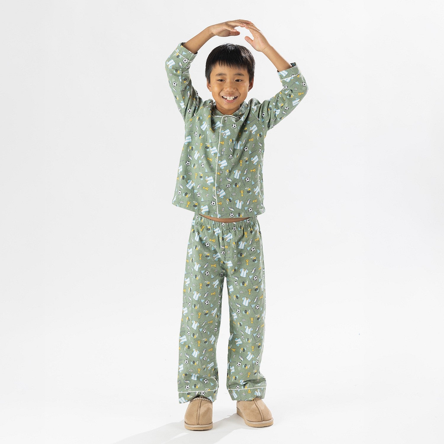 Child wearing green soccer print pyjamas standing on a white background.