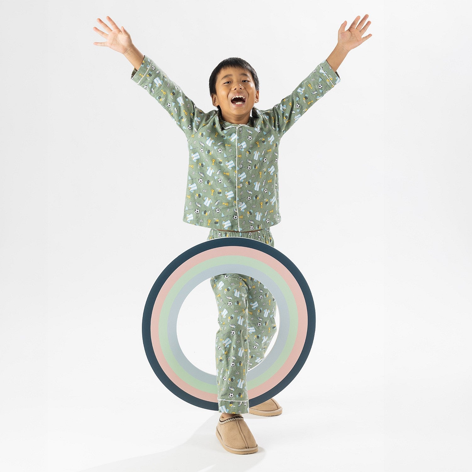 Child wearing green soccer print pyjamas standing on a white background.