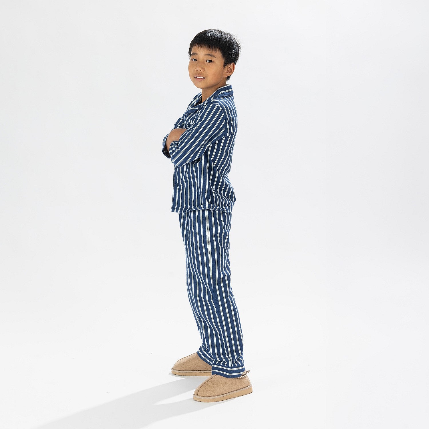 Child wearing blue striped flannelette pyjamas standing with his arms crossed