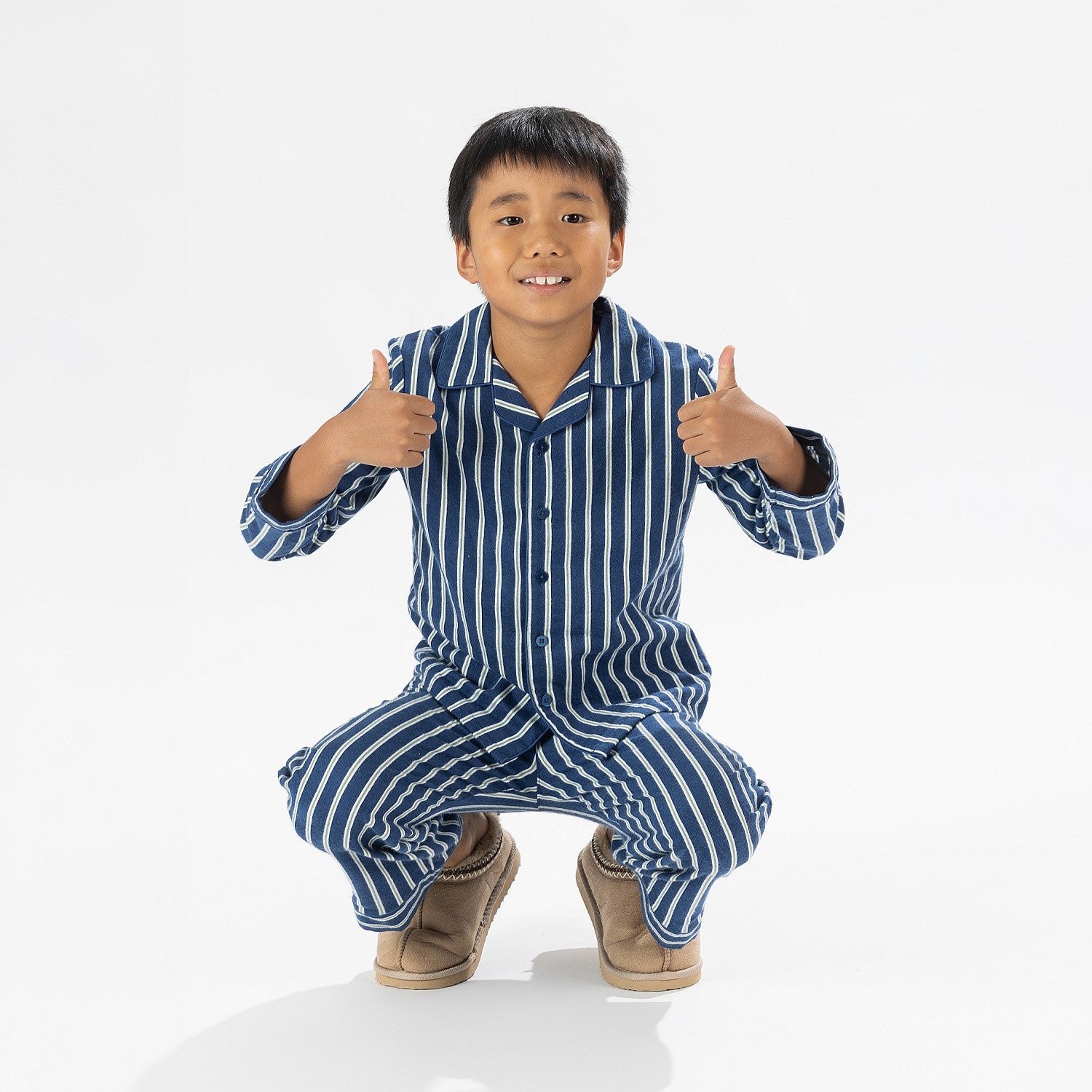 Child wearing blue striped flannelette pyjamas squating with his thumbs up 