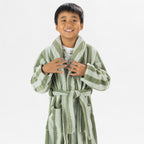 Child wearing a green striped robe standing on a white background.