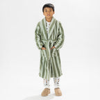 Child wearing a green striped robe standing on a white background.