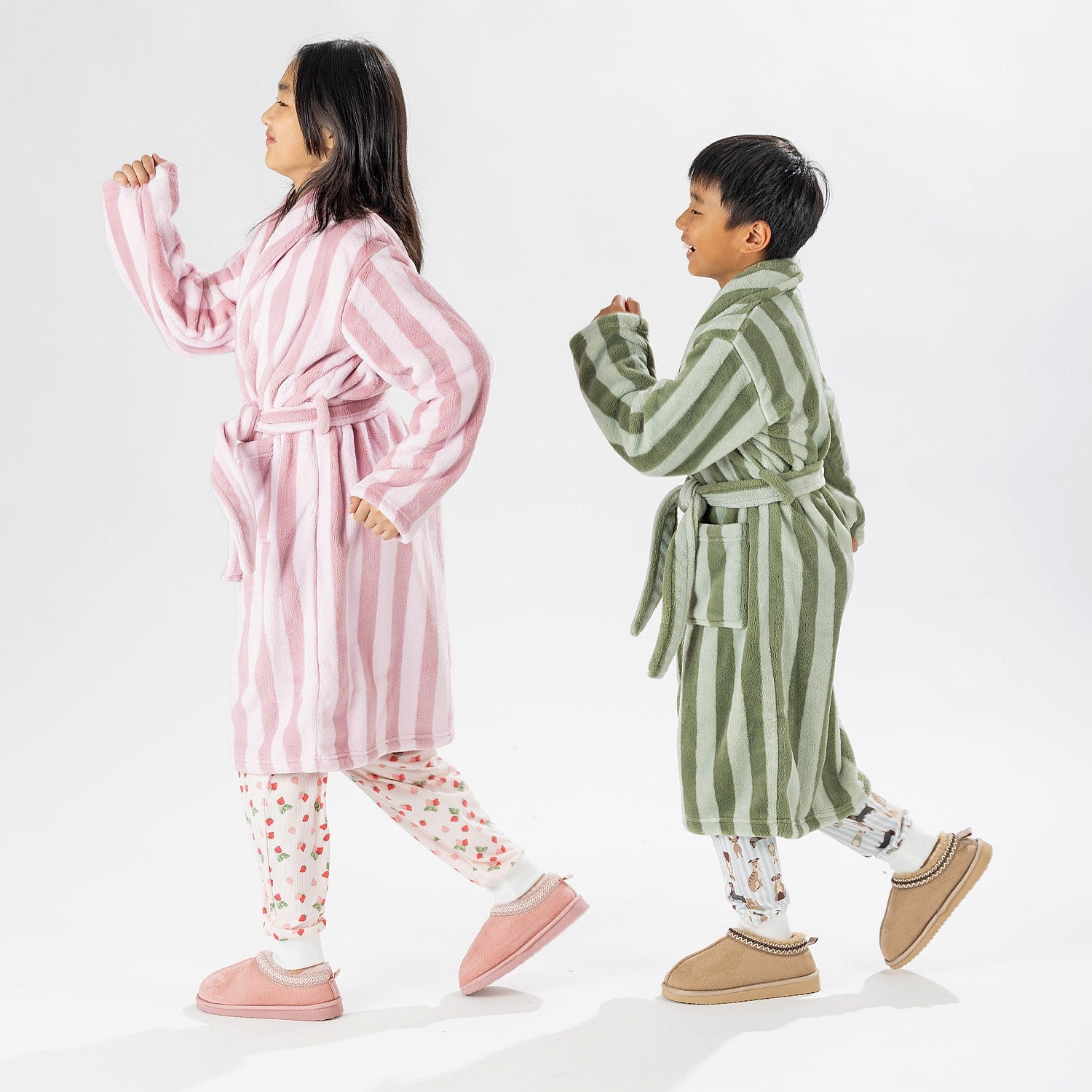 Two children wearing striped robes, one in pink and one in green, standing on a white background.